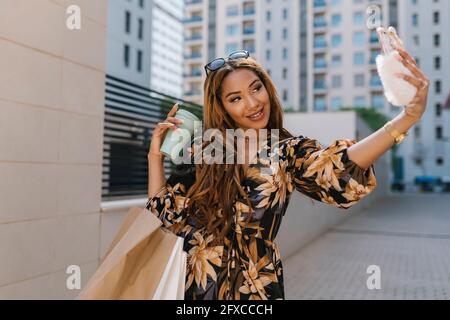 Schöne Frau hält Kaffeetasse und nimmt Selfie auf dem Smartphone auf dem Fußweg Stockfoto