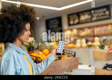 Afro-Frau, die mobile Anwendung im Lebensmittelgeschäft verwendet Stockfoto