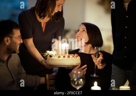 Überrascht Frau Blick auf weibliche Freundin hält Geburtstagskuchen zu Hause Stockfoto