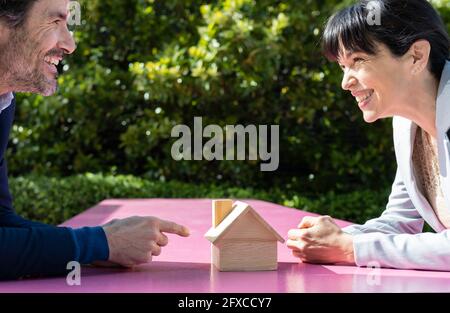 Lächelnder Immobilienmakler mit Modellhaus, das einen glücklichen Geschäftsmann anschaut Stockfoto