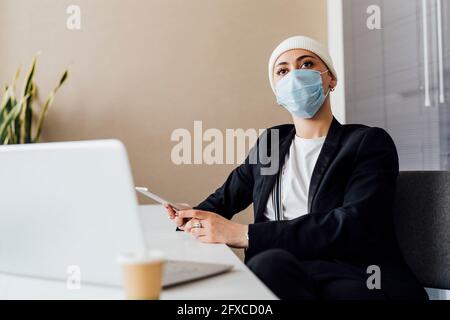 Junge Geschäftsfrau mit schützender Gesichtsmaske bei der Besprechung im Büro Stockfoto