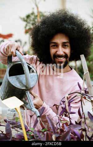 Lächelnder Mann, der Pflanzen im Garten wässert Stockfoto