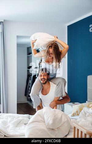 Fröhliche junge Frau mit Kissen Kampf mit Freund im Schlafzimmer Stockfoto