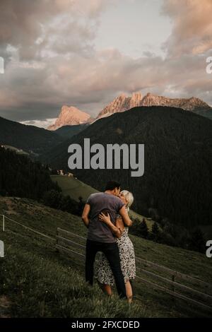 Paar umarmt, während sie auf Gras in der Nähe der dolomitenberge in Südtirol, Italien, steht Stockfoto