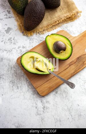 Studioaufnahme einer halbierten Avocado, die auf dem Schneidebrett liegt Stockfoto