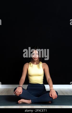 Schöne Sportsperson sitzt mit gekreuzten Beinen auf Trainingsmatte im Yoga-Studio Stockfoto