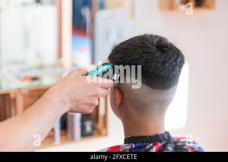 Männlicher Friseur, der im Friseurladen die Frisur eines Teenagers mit einem Gerät macht Stockfoto