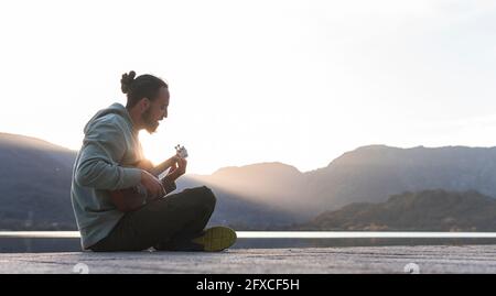 Junger Mann singt während des Sonnentages Ukulele auf der Promenade Stockfoto