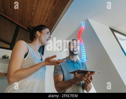 Physiotherapeutin und überraschte weibliche Patientin beim Blick auf holographisches anatomisches Modell der Wirbelsäule Stockfoto