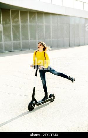 Verspielte Frau Reiten Elektroroller auf der Straße während sonnigen Tag Stockfoto