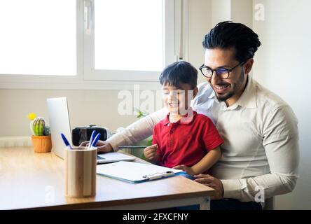 Geschäftsmann und Sohn lächeln, während sie zu Hause auf Clipboard schauen Stockfoto