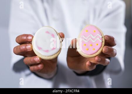 Weibliche Bäckerin hält rosa und weiße Creme Cracker in der Küche Stockfoto