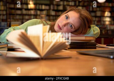 Frau starrte, während sie sich an den Tisch in der Bibliothek entspannte Stockfoto
