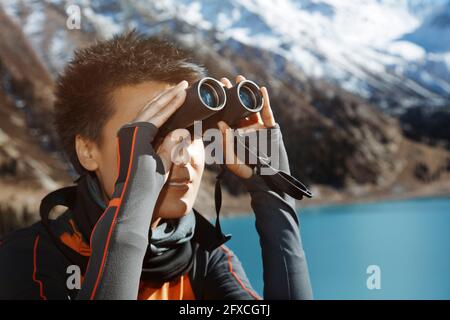 Frau mittleren Erwachsenen, die während der Ferien durch ein Fernglas am See schaut Stockfoto