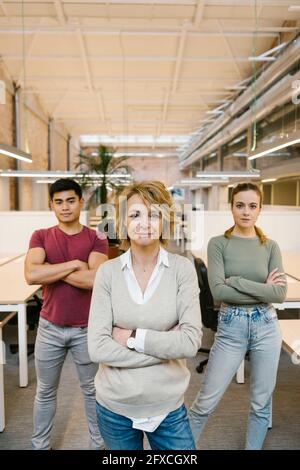 Männliche und weibliche Profis mit gekreuzten Armen stehen im Coworking-Büro Stockfoto