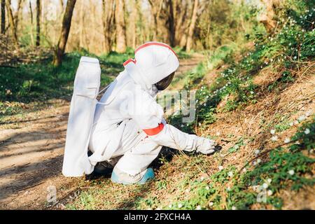 Weibliche Forscherin im Weltraum Anzug berühren Blume am Wald Stockfoto