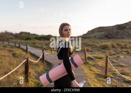 Frau mit Trainingsmatte, die über die Schulter schaut, während sie auf dem Fußpfad steht Stockfoto