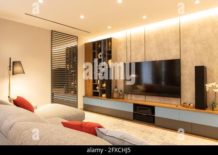 Modernes Wohnzimmer mit großem Sofa mit Ottomane, TV, offenem Abstellraum. Das Konzept ist trendige Innenausstattung in minimalistischem Stil, natürliche Materialien i Stockfoto