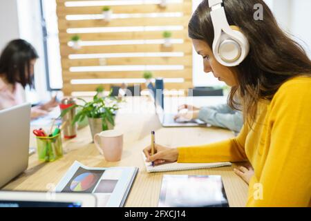 Professionelle Frau, die Kopfhörer trägt und im Büro schreibt Stockfoto