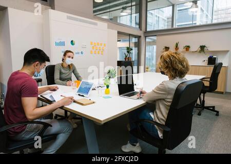 Männliche und weibliche Unternehmer diskutieren während einer Pandemie am Schreibtisch Stockfoto