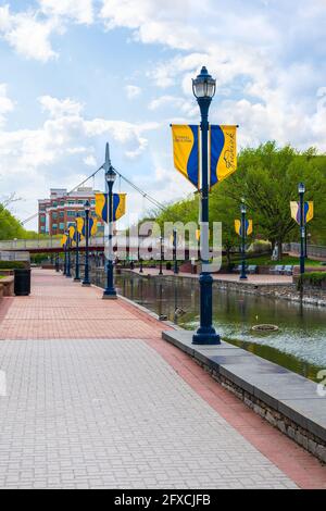 Carroll Creek Park im Herzen der Innenstadt von Frederick, Maryland mit einem gepflasterten Spaziergang entlang des Baches und Fahnen auf den Leuchtpfosten Stockfoto