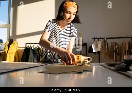 Professionelle weibliche Kanalisation machen Kleidungsproben im Studio mit Elektro Fräser auf Tisch in der Werkstatt Stockfoto