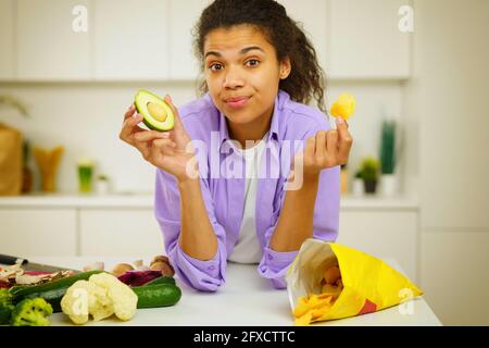 Der junge Koch in der Küche ist verwirrt, um Avocado zu essen Oder Billigvorsprünge Stockfoto