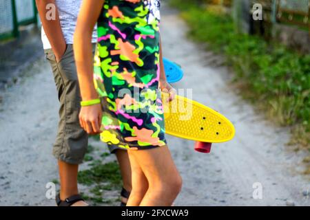 Unschärfe-Effekte für Kinder mit gelben und blauen Penny-Boards. Seitenansicht. Jugend-Hipster-Kultur. Nahaufnahme Kinderhände halten kurze Cruiser Pennyboard im Freien Stockfoto