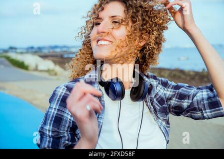 Nahaufnahme Porträt einer lächelnden, lockigen kaukasischen Frau mit großen Kopfhörern, die im Freien läuft. Genießen Sie den Moment und die Musik. Freiheit und Glück Stockfoto