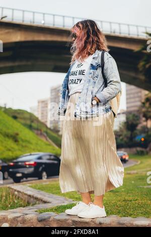 Modisch gekleidete, abendfüllende Feministin mit einer Brücke im Hintergrund. Vertikales Bild Stockfoto