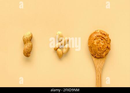 Erdnüsse und Erdnussbutter in Bambuslöffel aus Holz auf beige Hintergrund Stockfoto
