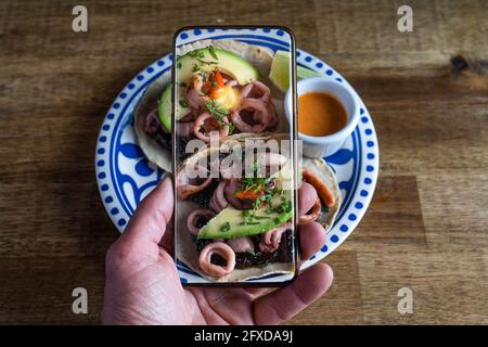 Mann, der Fotos von mexikanischem Essen auf dem Tisch gemacht hat. Tintenfisch-Tacos. Stockfoto