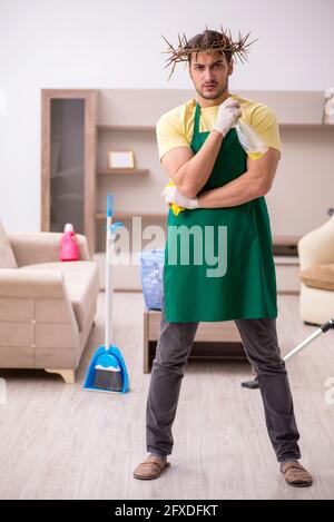 Junger männlicher Auftragnehmer, der auf dem Kopf einen stacheligen Kranz trägt und Hausarbeit leistet Stockfoto