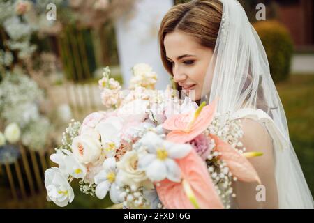 Romantische und schöne Frau in weißem Brautkleid mit einem großen frischen Strauß rosa und weißen Blumen in den Händen. Junge moderne Braut im Freien Stockfoto