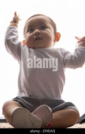 Ein kleines, niedliches und entzückendes kleines lateinisches Mädchen mit erhobenen Händen j, das Spaß hat, trägt lässige Kleidung in einem Studio, Expression Stockfoto