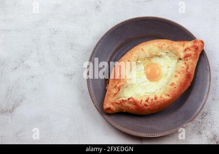 Traditionelles georgisches Käsegebäck Ajarian khachapuri auf einem runden Teller auf hellgrauem Hintergrund. Draufsicht, flach liegend Stockfoto