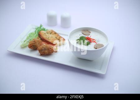 Creme der Pilzsuppe in einer weißen Schüssel mit angeordnet Geröstetes Brot und frischer grüner Gemüse-Salat als Beilage Auf einem weißen Servierbrett mit Weißwein angeordnet Stockfoto