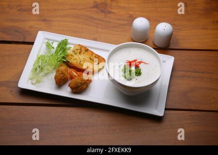 Creme der Pilzsuppe in einer weißen Schüssel mit angeordnet Geröstetes Brot und frischer grüner Gemüse-Salat als Beilage Auf einem weißen Servierbrett mit Holz angeordnet Stockfoto