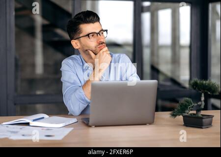 Nachdenkliche erfolgreiche, gutaussehende junge kaukasische Geschäftsführerin, Managerin oder Maklerin in formeller Kleidung und Brille, sitzend an einem Laptop im Büro, zur Seite schauend, seinen Kopf auf seine Hand ruhend Stockfoto