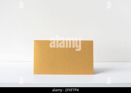 Goldene Einladungs- oder Grußkarte auf weißem Schreibtisch, beigefarbene Einrichtung. Leeres quadratisches Papierblatt auf dem leeren Tisch. Mockup, Platz für Text. Stockfoto