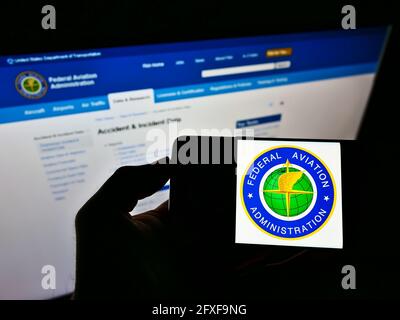 Person, die das Smartphone mit dem Siegel der US-amerikanischen Federal Aviation Administration (FAA) auf dem Bildschirm vor der Website hält. Konzentrieren Sie sich auf die Telefonanzeige. Stockfoto