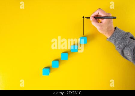 Man Hand Zeichnung einen nach oben zeigenden Pfeil auf der wachsenden Grafik aus Holzblock. Auf gelbem Hintergrund Stockfoto