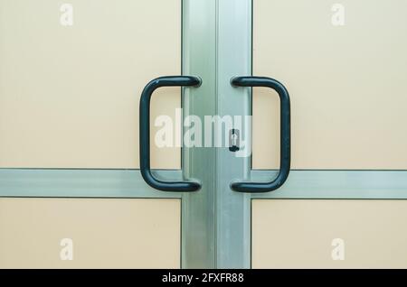 Vordertür aus Aluminium mit bogenförmigen Griffen. Beige, blickdichte Tür mit schwarzen Griffen. Notausgang. Schießen im Regen. Regentropfen. Stockfoto