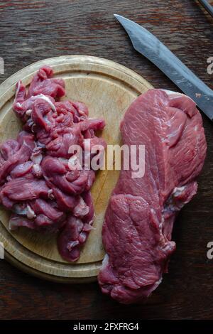 Stücke von rohem Rindfleisch auf einem runden Schneidebrett. Ganze Stücke Rinderfilet und zerfetzt in Streifen für Befstrangonovs Stockfoto