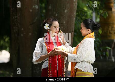 Zwei Frauen aus Myanmar halten Blumen in einem Tempel. Südostasiatische junge Mädchen mit burmesischen traditionellen Kleidern besuchen einen Buddihist Stockfoto