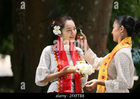 Zwei Frauen aus Myanmar halten Blumen in einem Tempel. Südostasiatische junge Mädchen mit burmesischen traditionellen Kleidern besuchen einen Buddihist Stockfoto