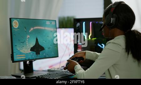 Pro african Gamer spielen Online-Weltraum-Shooter-Spiel auf einem leistungsstarken Computer mit Wireless-Controller und Headset. Wettbewerbsfähige Cyber-Spieler Frau Durchführung Videospiel-Turnier verwenden professionelle Joystick Stockfoto