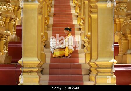 Frauen aus Myanmar halten Blumen an einem Tempel. Südostasiatische junge Mädchen mit burmesischen traditionellen Kleidern besuchen einen Buddihist-Tempel Stockfoto