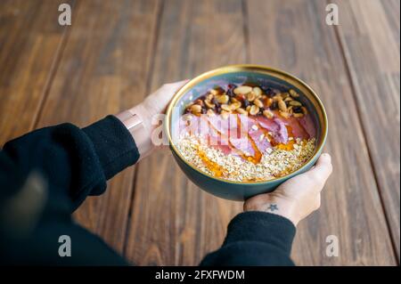 Smoothie-Schüssel mit Mango und Beeren mit den Händen halten Holztisch Stockfoto