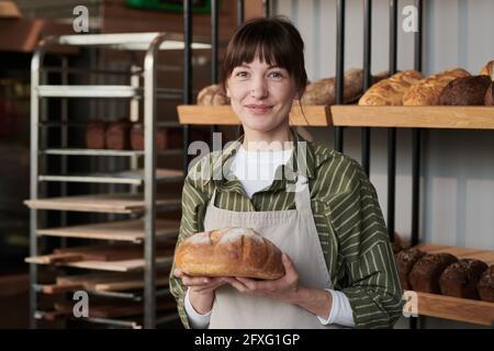 Porträt einer jungen Frau in Schürze mit frischem Brot suchen Bei der Kamera in der Bäckerei Stockfoto